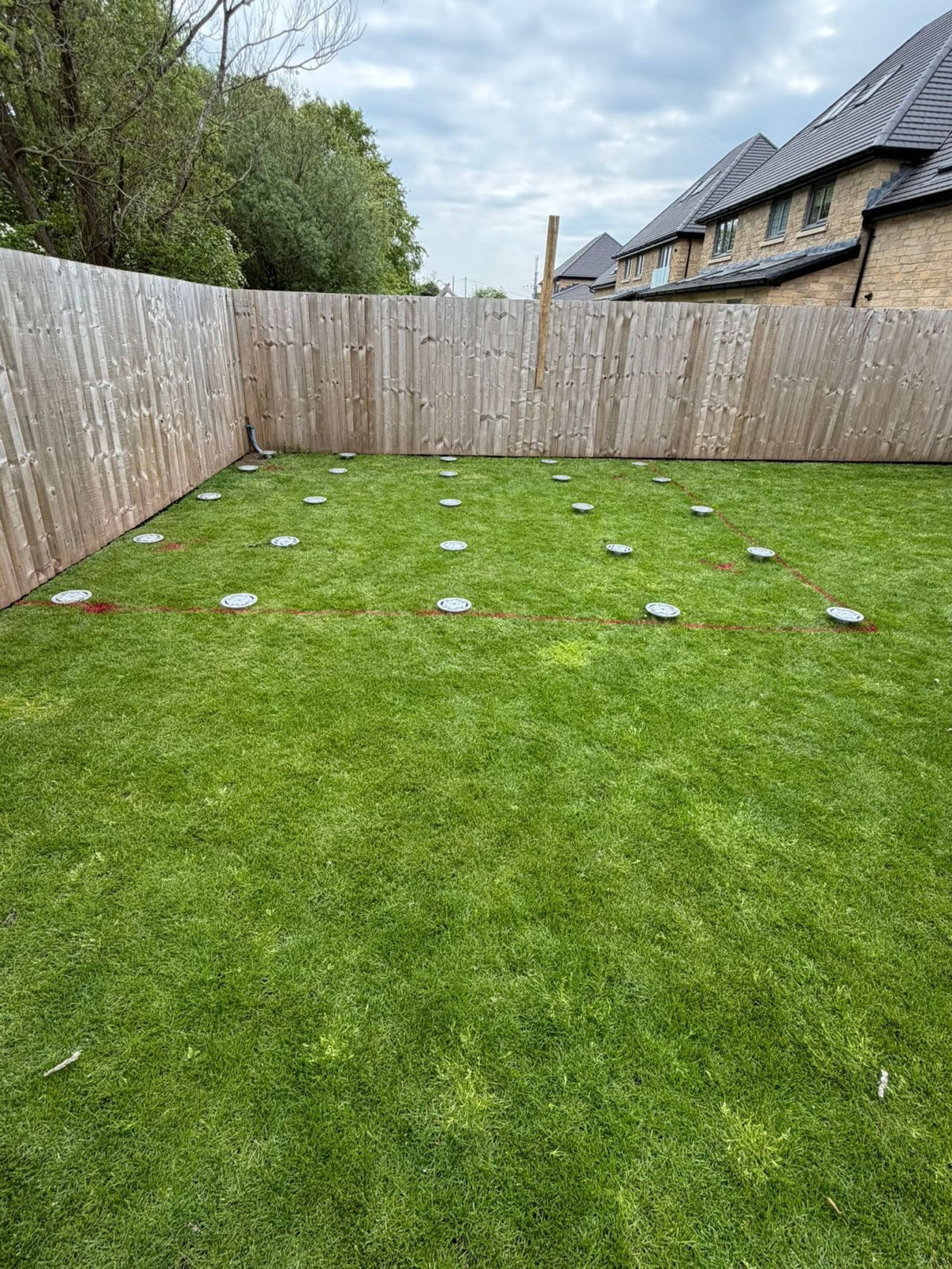 Installed ground screw heads arranged across a garden foundation footprint